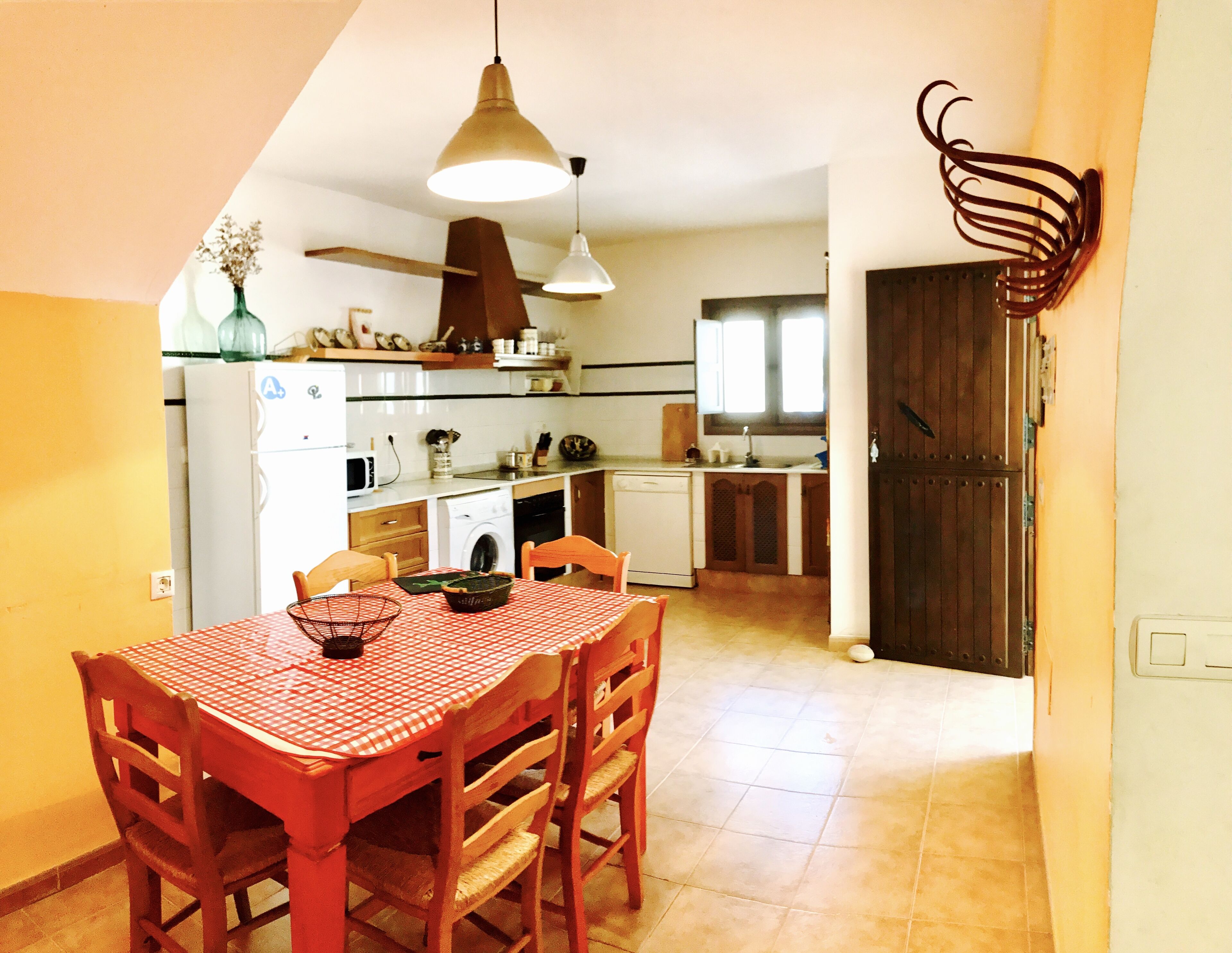 A compact kitchen with a dining table, chairs, and a hanging light fixture.