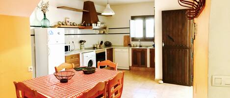 A compact kitchen with a dining table, chairs, and a hanging light fixture.