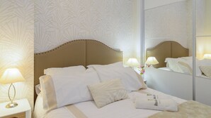 Et hotelværelse med en seng, to sengeborde med lamper, et spejl og en blomsterdekoration.