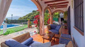 Um pátio coberto com móveis de vime, piscina e vista para as montanhas.