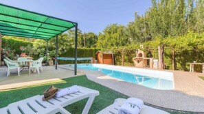 Een zwembad met een overdekt terras, buitenmeubels en een kleine tuin.