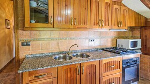 A kitchen with wooden cabinets, a granite countertop, a sink, a microwave, and a stove. - Casa Rural Pelijas Fontanar by Ruralidays (Jaén)