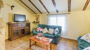A living room with a sofa, a wooden coffee table, a television on a cabinet, and a window with curtains. - Casa Rural Pelijas Fontanar by Ruralidays (Jaén)