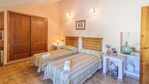 A bedroom with two beds, a nightstand, a lamp, a painting, and a small table with decorative items. - Casa Rural Pelijas Fontanar by Ruralidays (Jaén)