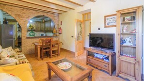 A living room with a television, wooden furniture, a dining area, and a kitchen with an arched brick feature. - Casa Rural Pelijas Fontanar by Ruralidays (Jaén)