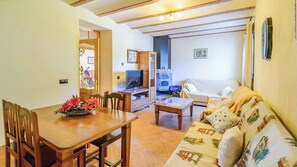 A dining area with a wooden table and chairs, a sofa with patterned cushions, a television, and a kitchen area with a stove and oven. - Casa Rural Pelijas Fontanar by Ruralidays (Jaén)