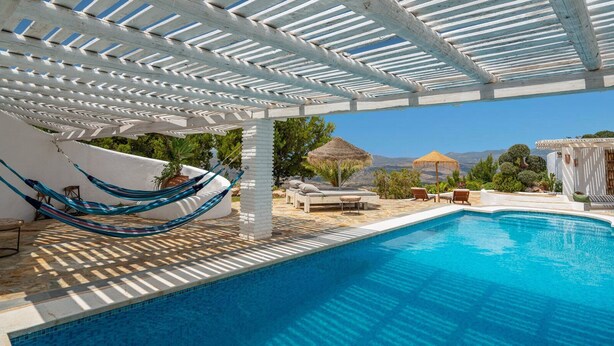Un área de piscina con una pérgola blanca, una hamaca y sillas de descanso.