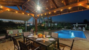 Uma área de refeições ao ar livre com piscina, deck de madeira e um espaço de estar coberto.