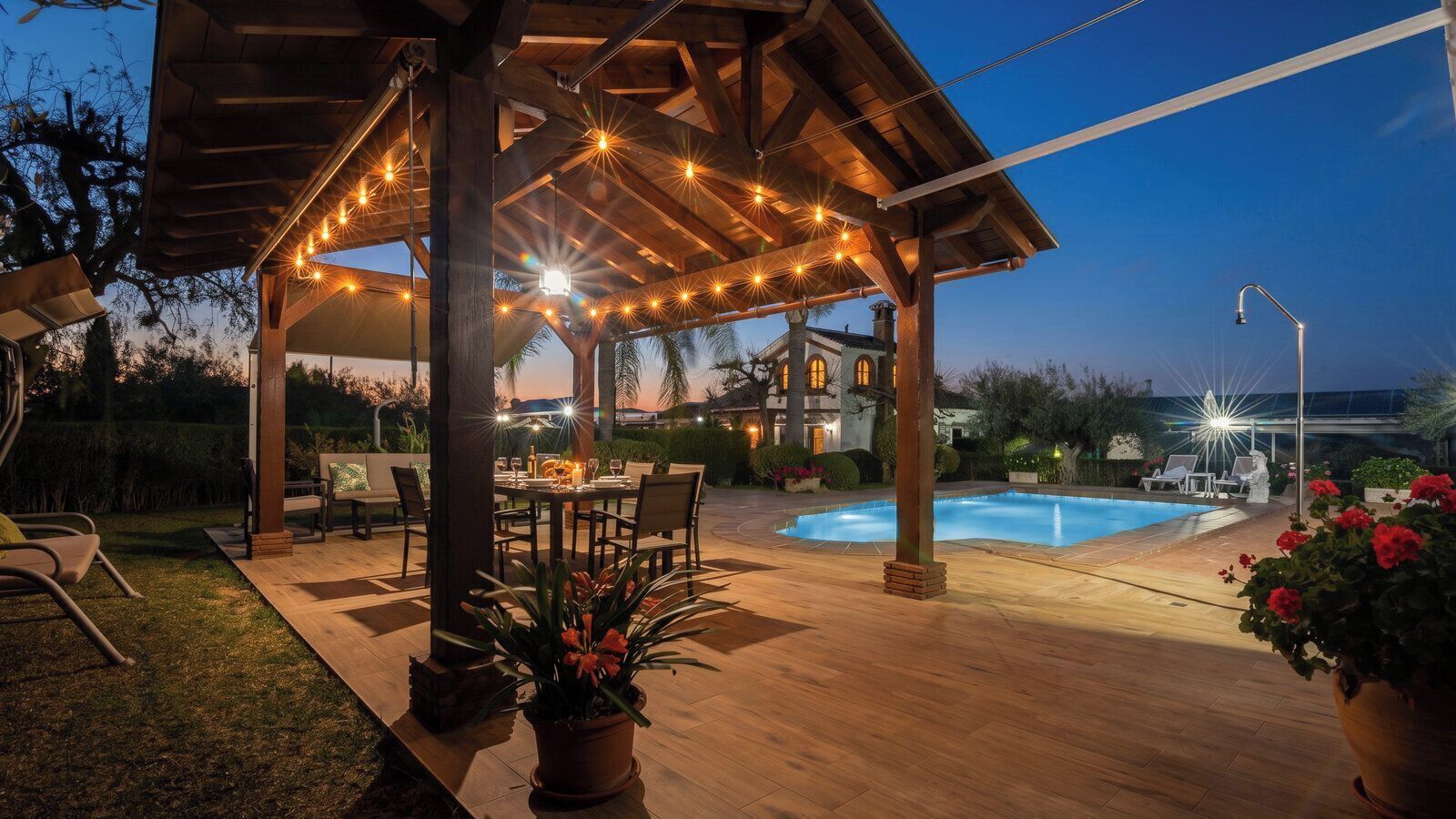 Une terrasse extérieure avec une piscine, un plancher en bois et des guirlandes lumineuses.