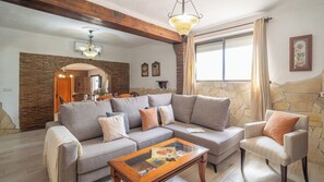 A living room with a sectional sofa, a chair, a coffee table, a fireplace, and a stone wall. - Casa Maza de Guaro by Ruralidays (Málaga)