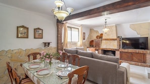 A dining area with a stone wall, a fireplace, and a television in the living room. - Casa Maza de Guaro by Ruralidays (Málaga)
