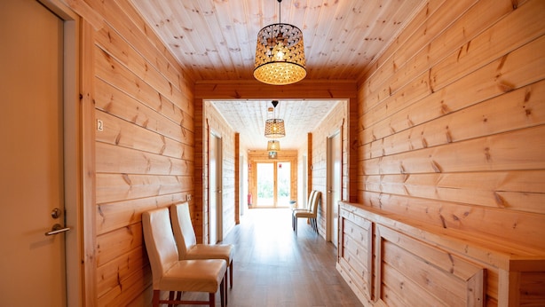 A wooden hallway with two chairs on the left, a door on the left, and a door at the end. - Glaðheimar Guesthouse (Blönduós)