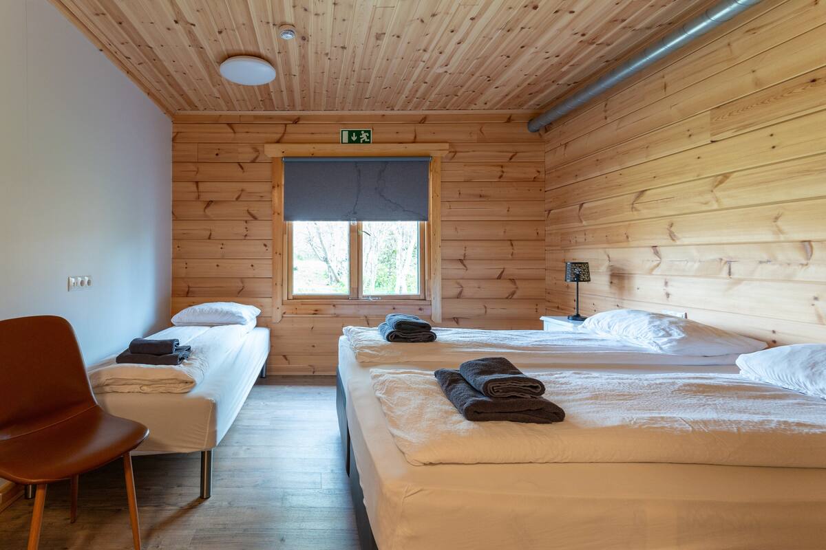 Une chambre de style cabane avec deux lits, un plafond en bois, une fenêtre et une chaise.