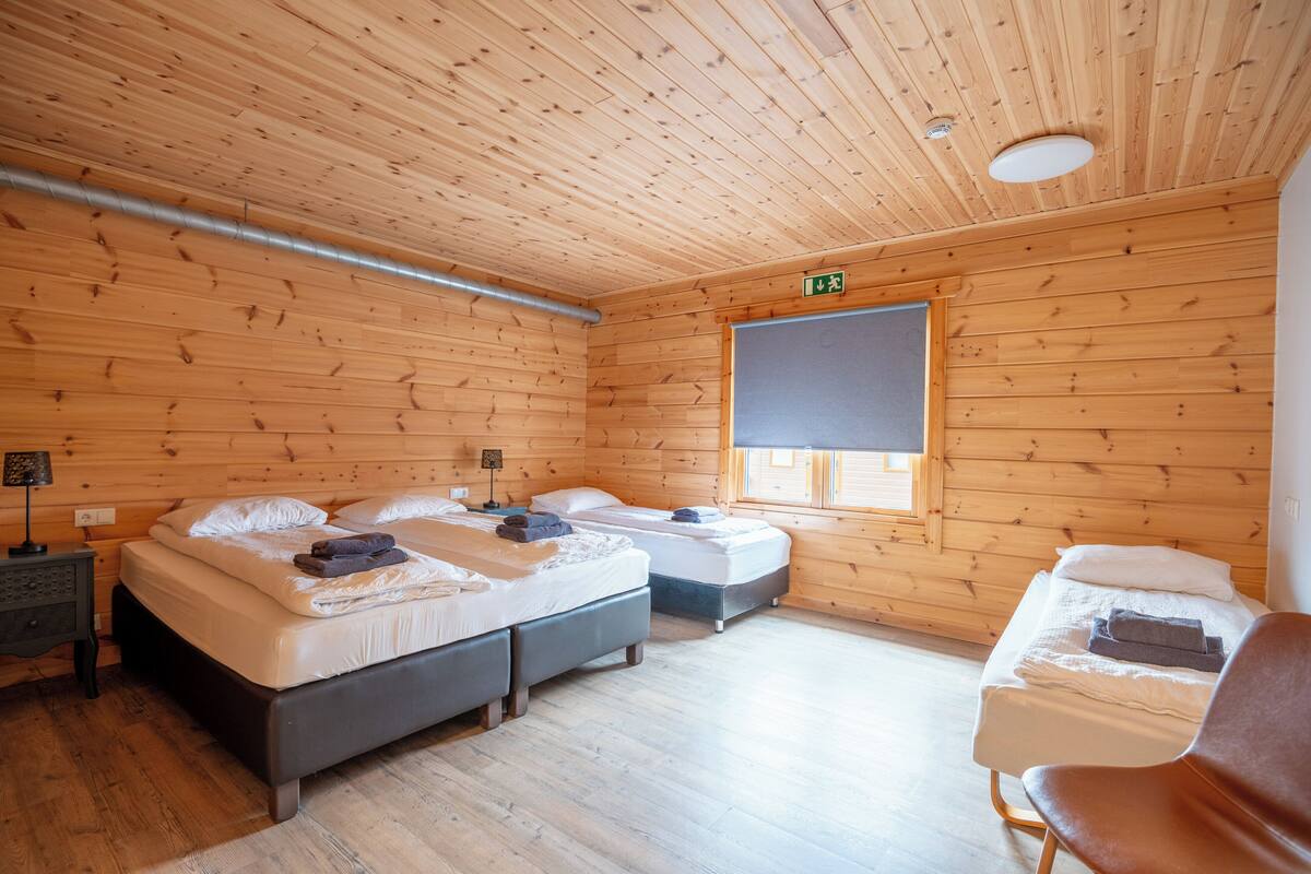 Une pièce de cabane en bois avec deux lits, un banc et une fenêtre.