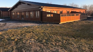A wooden building with a sloped roof and large windows, surrounded by a grassy area. - Glaðheimar Guesthouse (Blönduós)