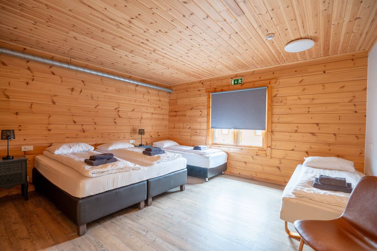 A wooden cabin room with two beds, a bench, and a window.
