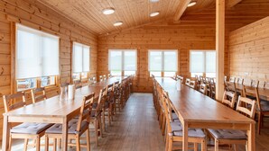 A large wooden dining hall with long tables and chairs, large windows, and a high wooden ceiling with recessed lighting. - Glaðheimar Guesthouse (Blönduós)