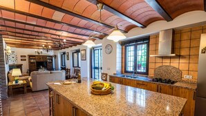 A spacious kitchen with granite countertops, wooden cabinets, and a large island. There is a dining area with a sofa and a table, and a living room with a fireplace.