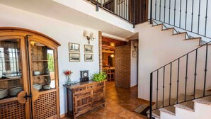 A spacious hallway with a wooden cabinet, a dining area with a brick wall, and a staircase with metal railings.