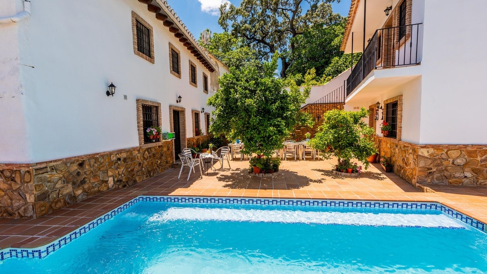 A swimming pool with a tiled edge, surrounded by stone walls and white buildings with balconies.