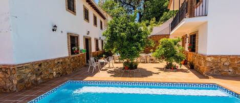 A swimming pool with a tiled edge, surrounded by stone walls and white buildings with balconies.