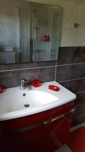 A bathroom with a white sink, red basin, and chrome faucet. There is a mirror above the sink and a shower area with a glass door. - La Garrinière (Saint-Raphael)