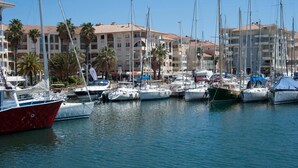 A marina with multiple sailboats docked, surrounded by multi-story buildings with balconies and palm trees. - La Garrinière (Saint-Raphael)