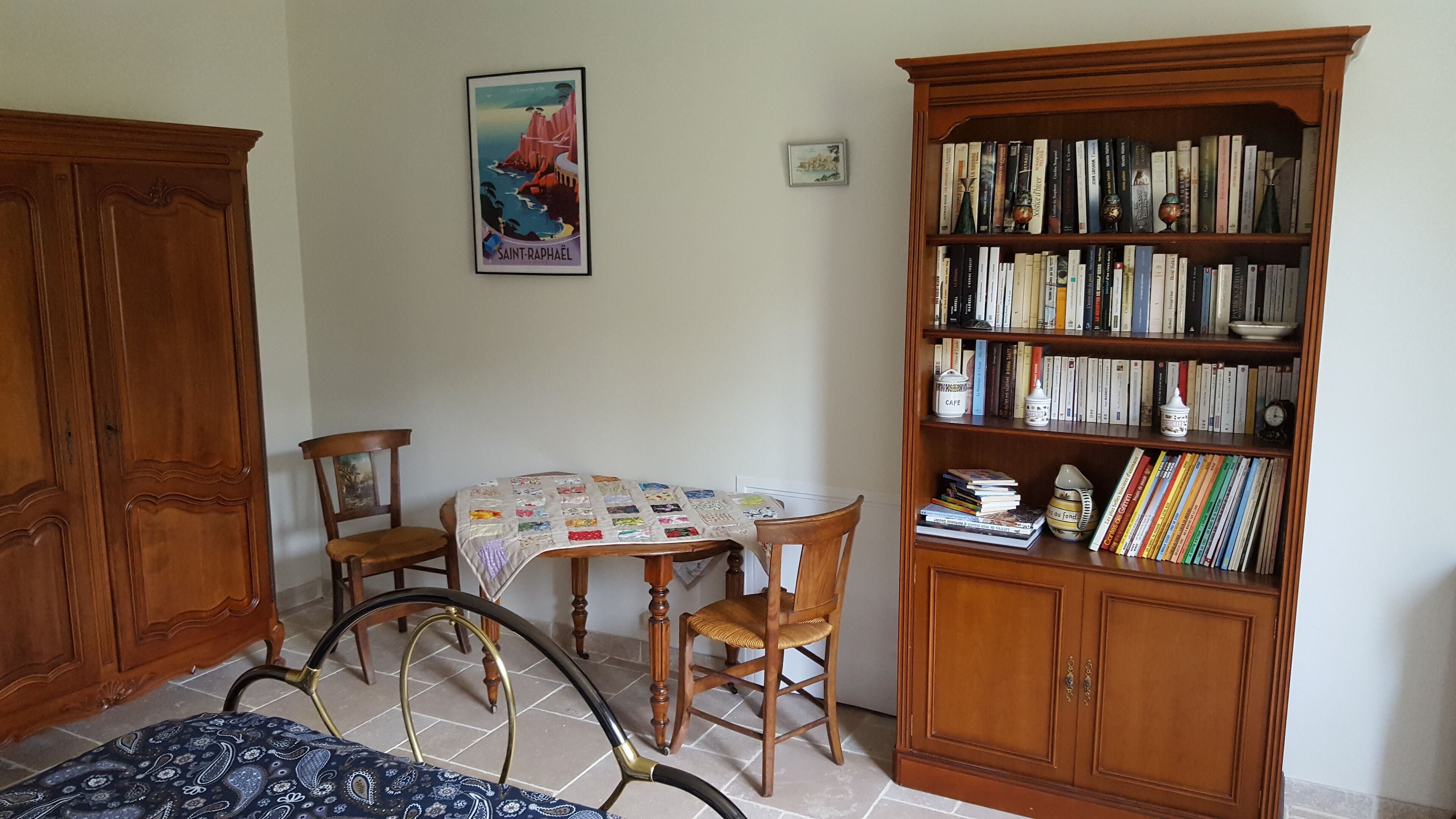 Una stanza con un armadio in legno, un tavolo con una coperta, due sedie e una libreria piena di libri.