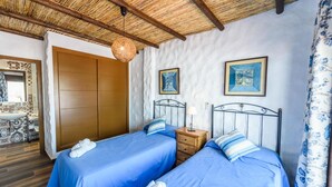 A bedroom with two beds, a wooden wardrobe, a hanging light fixture, and framed artwork on the wall.