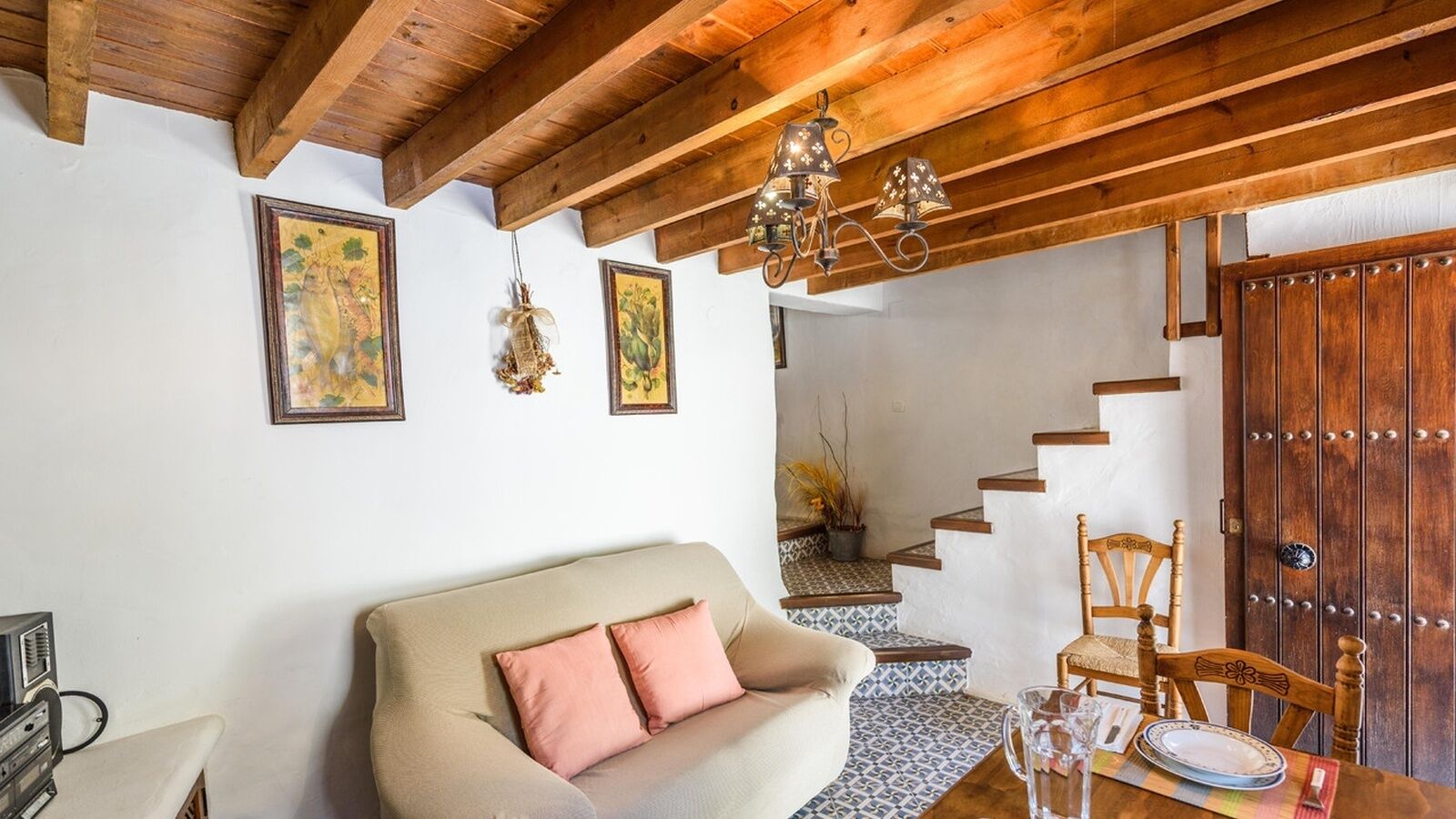 A cozy living room with a sofa, a wooden chair, a dining table with plates, and a staircase leading to another level.