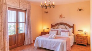 A bedroom with a wooden bed, two bedside tables, a chandelier, and a window with curtains. - Huerta Alejo Alozaina by Ruralidays (Málaga)