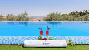A pool with a clear view of the surrounding landscape, a towel with 'runalidays' branding, and two drinks with strawberries.