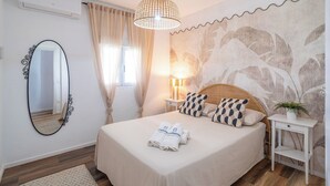 Uma cama bem arrumada com cabeceira, mesa de cabeceira com abajur, espelho e papel de parede com padrão de folhas.