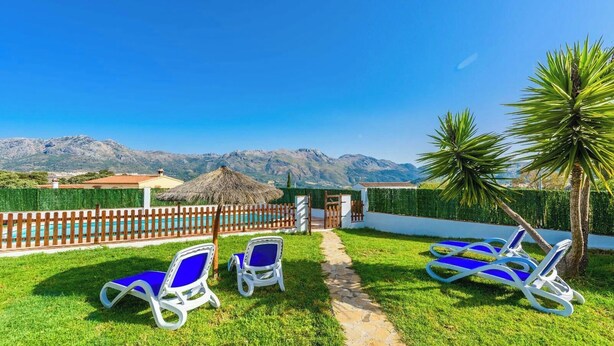 A poolside area with lounge chairs, a thatched umbrella, and a view of mountains.