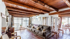 A cozy living room with a wooden ceiling, a sofa, and a dining area with wooden chairs and a table.
