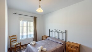 Une chambre avec un lit simple, une chaise en bois, une table de chevet et une fenêtre avec des rideaux.