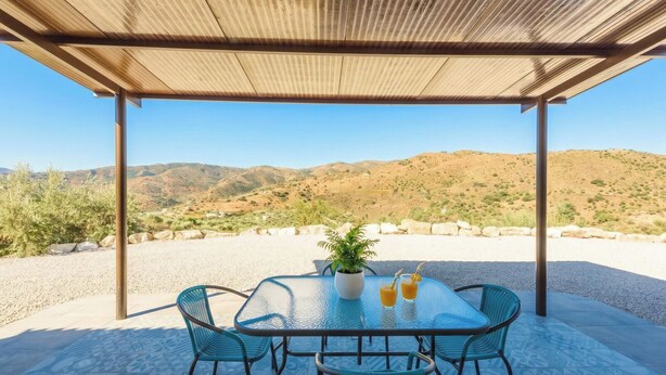 Un espace extérieur abrité, avec une table et des chaises, une plante en pot et deux boissons.