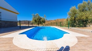 Une piscine rectangulaire avec une zone d’eau d’un bleu limpide, entourée d’une terrasse carrelée et d’une clôture verte.