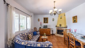A living room with a sofa, a dining table with chairs, a fireplace, and a television. - Cortijo Los Naranjos Frigiliana by Ruralidays (Málaga)