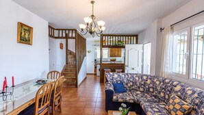 A spacious living area with a patterned sofa, a dining table with chairs, a kitchen in the background, and a staircase leading to another level. - Cortijo Los Naranjos Frigiliana by Ruralidays (Málaga)