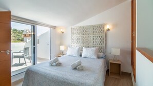 Ein Schlafzimmer mit einem Bett, zwei Nachttischen, einem dekorativen Kopfteil und einer Glastür, die auf einen Balkon führt.
