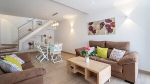 Ein modernes Wohnzimmer mit einem braunen Sofa, einem Holztisch und einem Essbereich mit weißem Tisch und Stühlen.
