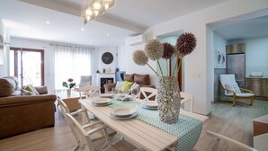 Ein modernes Wohnzimmer mit Essbereich, mit einem Holztisch gedeckt mit Tellern und Gläsern, einer dekorativen Vase und einer Couch mit Kissen.