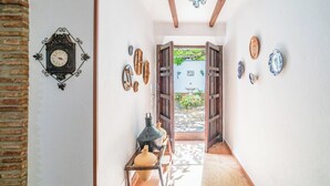 Ein schmaler Korridor im rustikalen Stil, mit einer an der Wand befestigten Uhr, verschiedenen dekorativen Tellern und einem Blick auf einen Garten durch eine offene Tür.