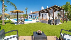 Ein Poolbereich mit Liegestühlen, einer überdachten Lounge und Blick auf die umliegende Landschaft.