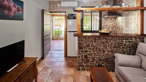 Une cuisine avec un mur en pierre, un comptoir en bois et un téléviseur posé sur un meuble en bois.