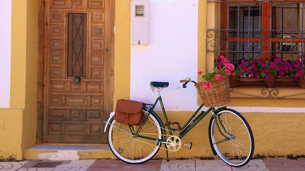 A bicycle parked next to a yellow building with a wooden door and a window with metal bars.