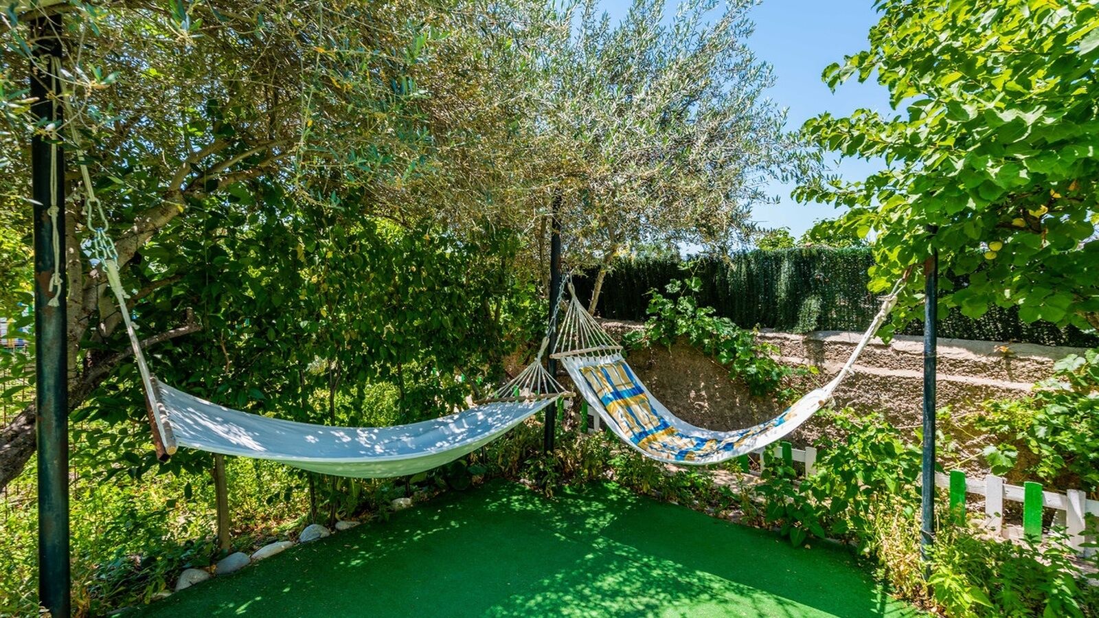 A hammock suspended between two poles in a garden with green grass and trees.