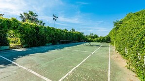 Ein Tennisplatz im Freien, umgeben von üppigem Grün und blauem Himmel.