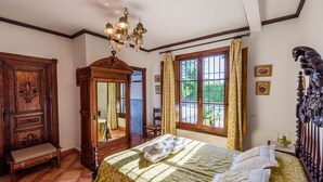 Ein Schlafzimmer mit einem großen Bett, einem Holzschrank, einem Spiegel und einem Fenster mit Vorhängen.